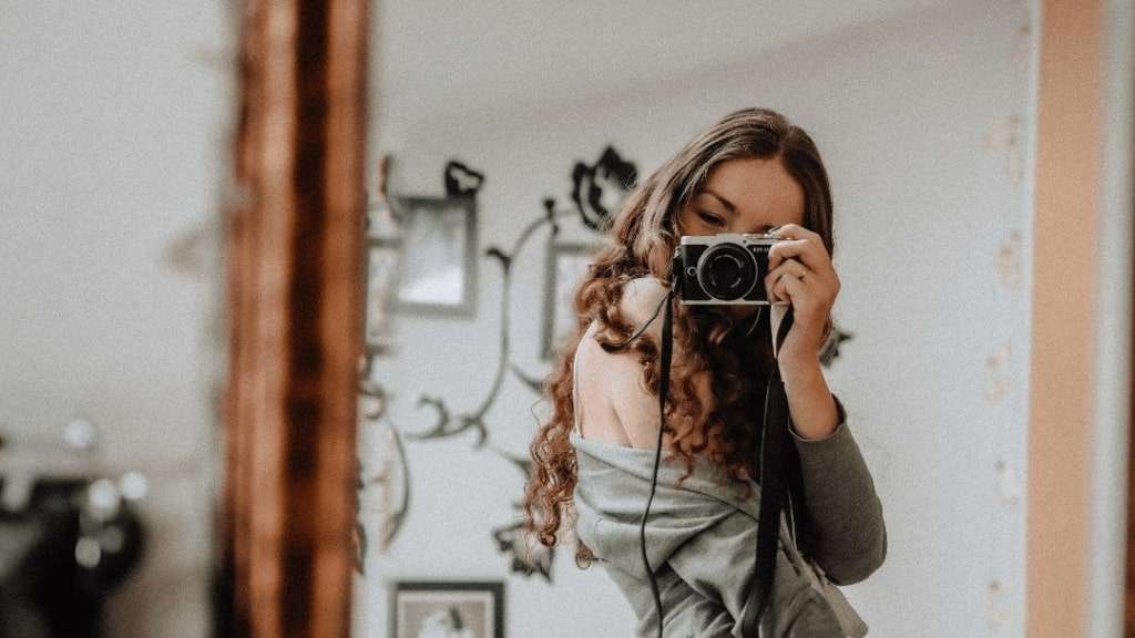 Happy carefree woman smiles gladfully holds camera as taking selfie poses  for making photo pulls wea Stock Photo by wayhomestudioo
